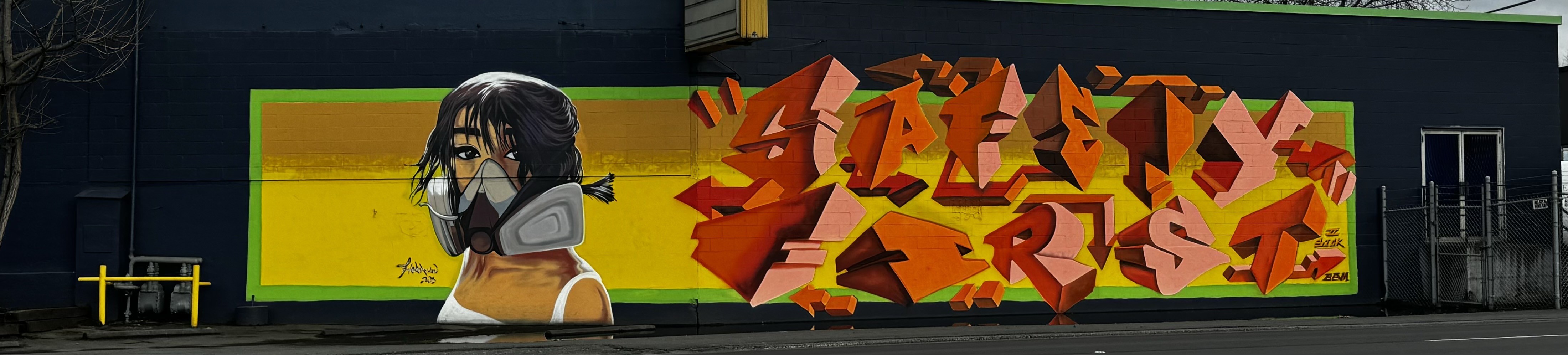 Street art of a woman wearing a respirator mask and block letter that read “safety first”. 