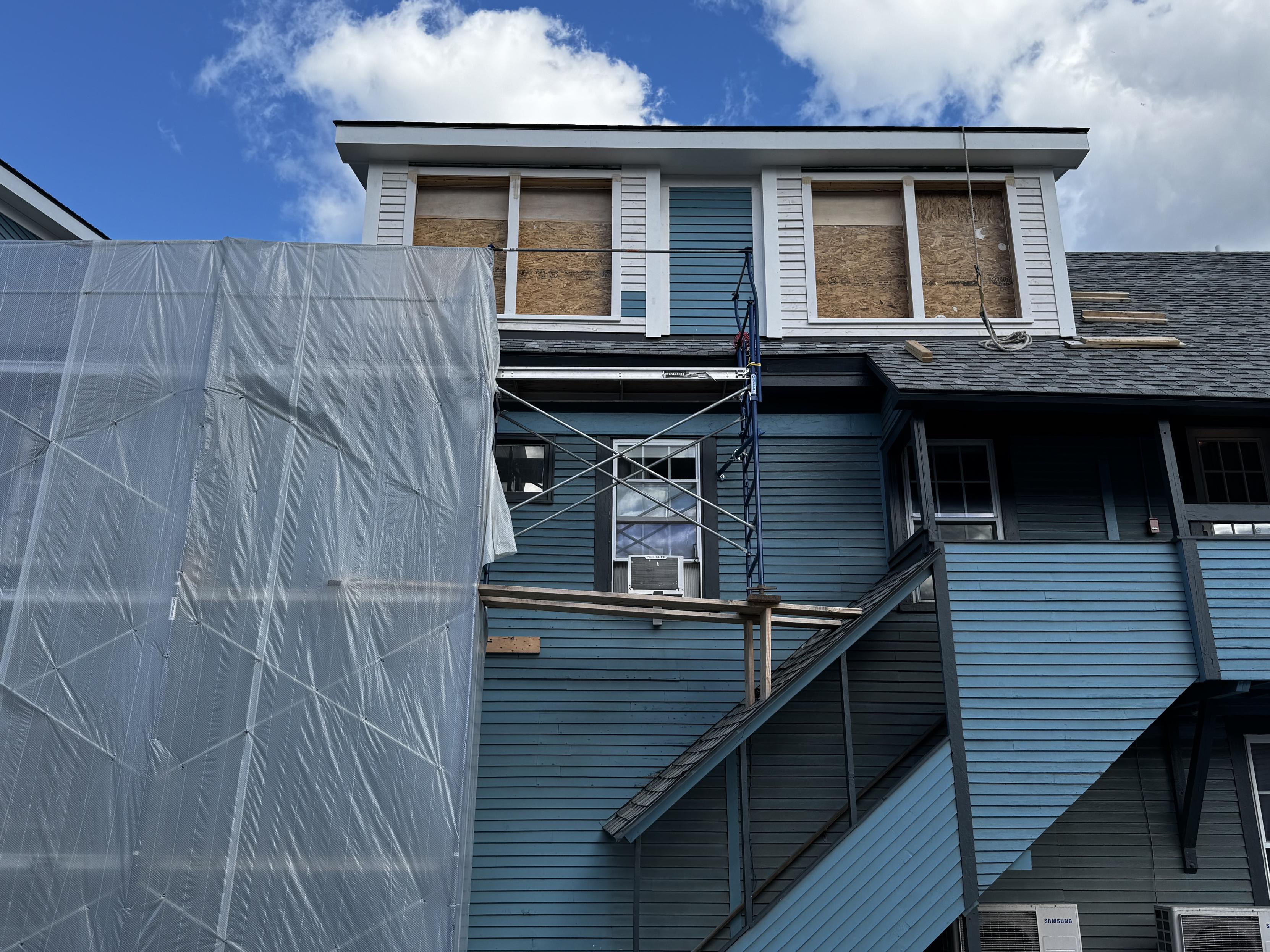 Photo of metal scaffolding supported by wood 2x6s resting at at 45 degree angle on the roof of a house.